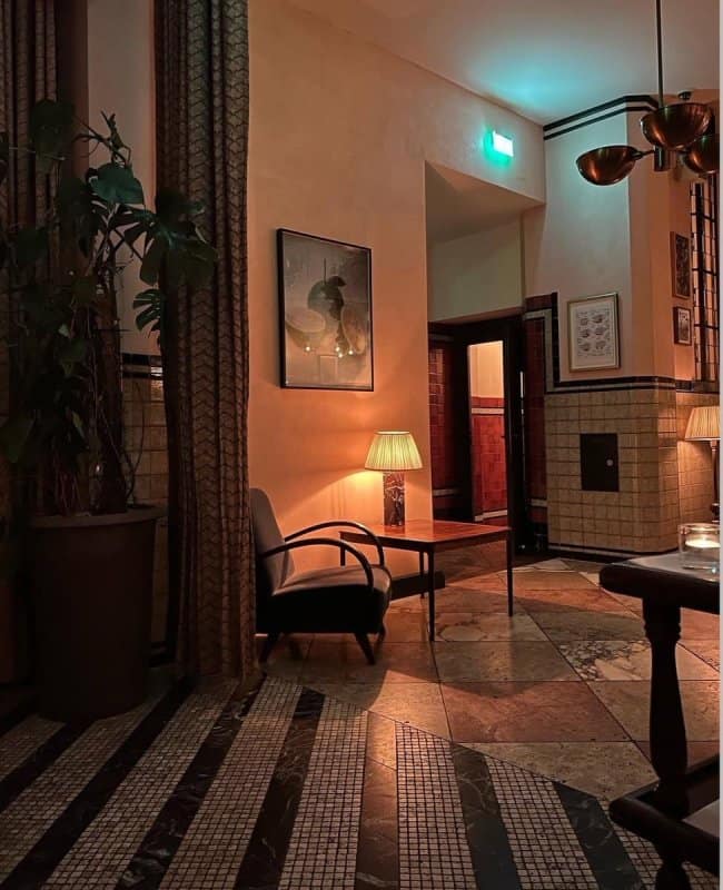 A moody awesome home decor lounge corner with vintage tiled walls, geometric flooring, and warm lamp lighting creating a sophisticated film noir atmosphere.