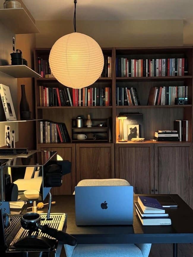 A sophisticated masculine home decor study room with floor-to-ceiling dark wood bookshelves, a minimalist desk setup, and a large Japanese paper lantern.