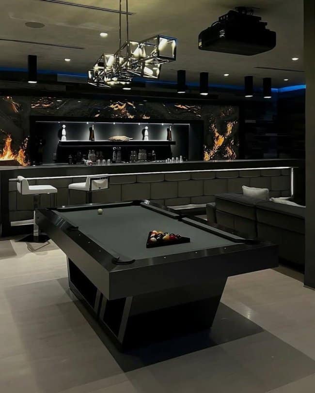 The ultimate masculine home decor entertainment room boasting a custom black-felt pool table, a fully stocked backlit bar, and a modern fireplace.