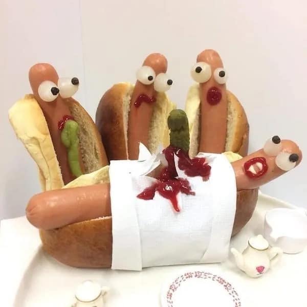 An incredibly creative and bizarre food art funny meme showing hotdogs with googly eyes reacting in absolute horror as one of their friends is dramatically split open on a tiny bun hospital bed, bleeding ketchup everywhere in this unhinged meme dump.