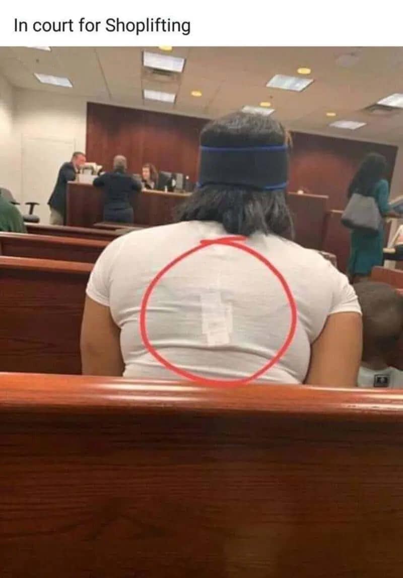 A meme dump photo of a woman in a courtroom with a security tag still stuck to the back of her white shirt.