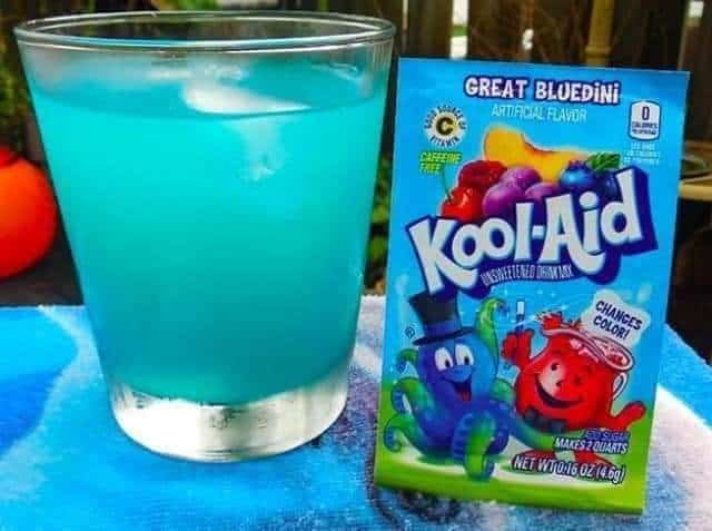 A glass of bright blue liquid next to a packet of Great Bluedini Kool-Aid, a magical nostalgic drink that changed color when mixed.
