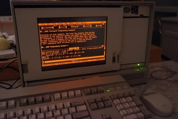 Retro computer with an orange monochrome display showing lines of code on the screen.