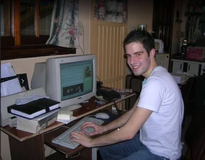 Young man smiling while sitting at a desk with a large beige CRT monitor.