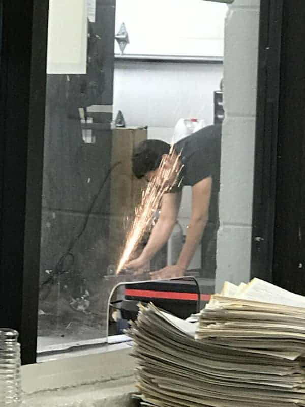 A classic funny osha fail waiting to happen, showing a worker grinding metal with a stream of hot sparks landing directly on a stack of dry paper.