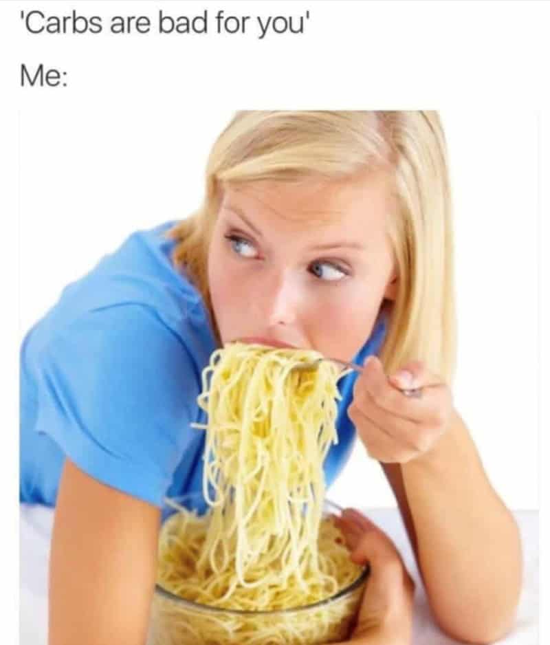 Woman in a blue shirt intensely eating a massive bowl of spaghetti with a fork.