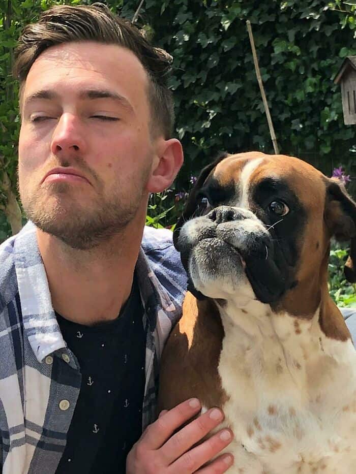 Man making a skeptical pouting face next to a boxer dog with a naturally similar muzzle.