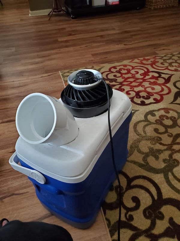 A redneck DIY air conditioner made from a blue cooler, a small fan, and a white PVC pipe elbow.