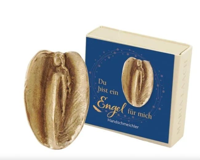 A golden "Angel for me" pocket charm in its blue gift box, suffering from a major unfortunate design where the stylized angel's wings and recessed body look remarkably accidentally nsfw.