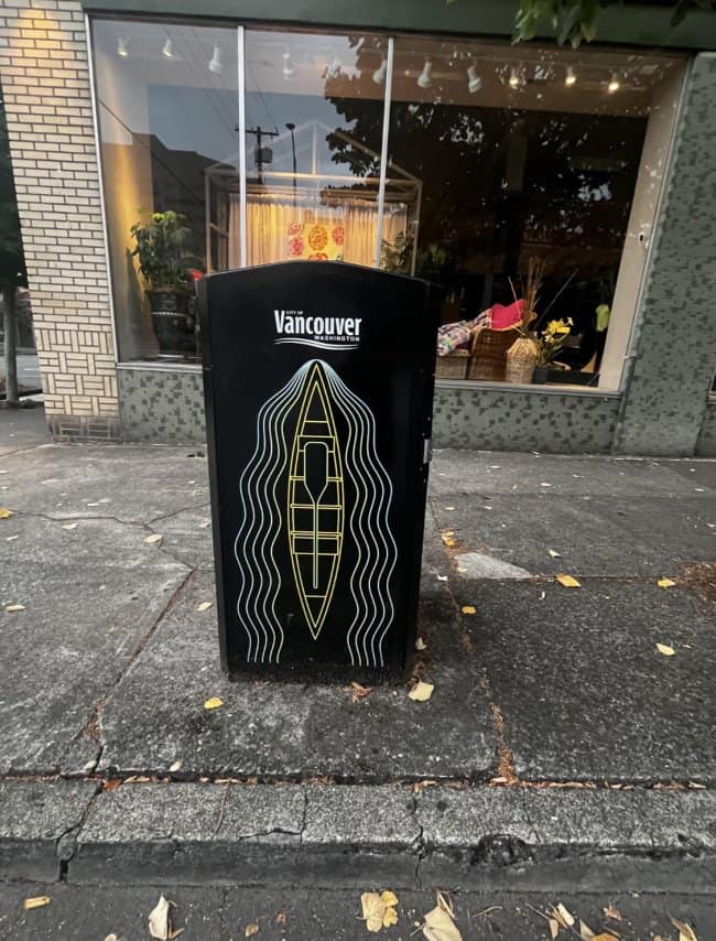 An unfortunate design on a Vancouver city trash can featuring a line-art logo of a yellow canoe surrounded by wavy water lines, unintentionally forming a massive and highly accidentally nsfw graphic.