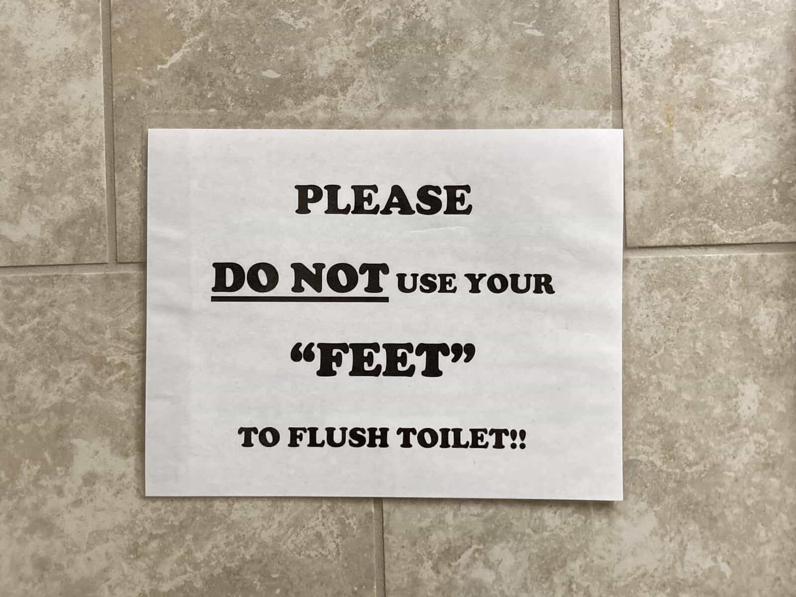 Restroom sign instructing users not to use their feet in quotation marks to flush toilets.