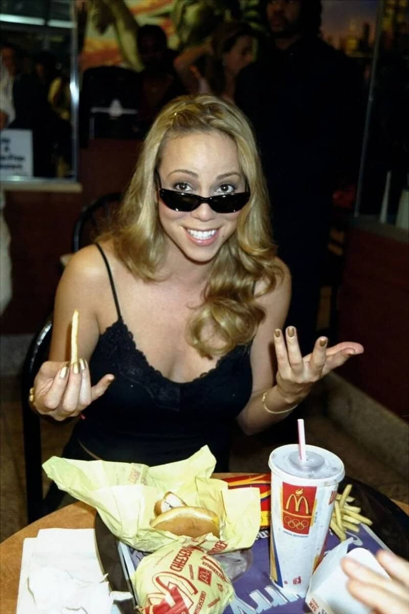 A vintage McDonalds image of a young Mariah Carey wearing sunglasses and eating a cheeseburger in the 90s.