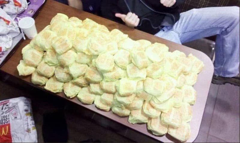 A vintage McDonalds image showing a massive mountain of 90s era cheeseburgers wrapped in yellow paper sitting on a table.