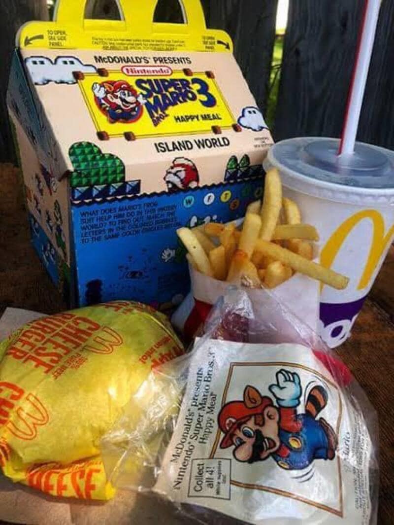 A vintage McDonalds image of a Super Mario Bros. 3 Happy Meal box from 1990 sitting next to fries and a burger.