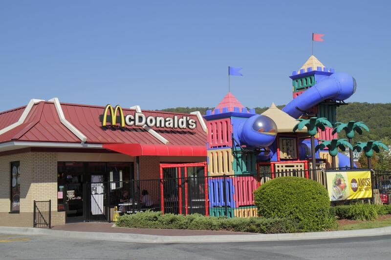 A vintage McDonalds image of an outdoor Playplace featuring a giant Grimace cage, Officer Big Mac, and slides.
