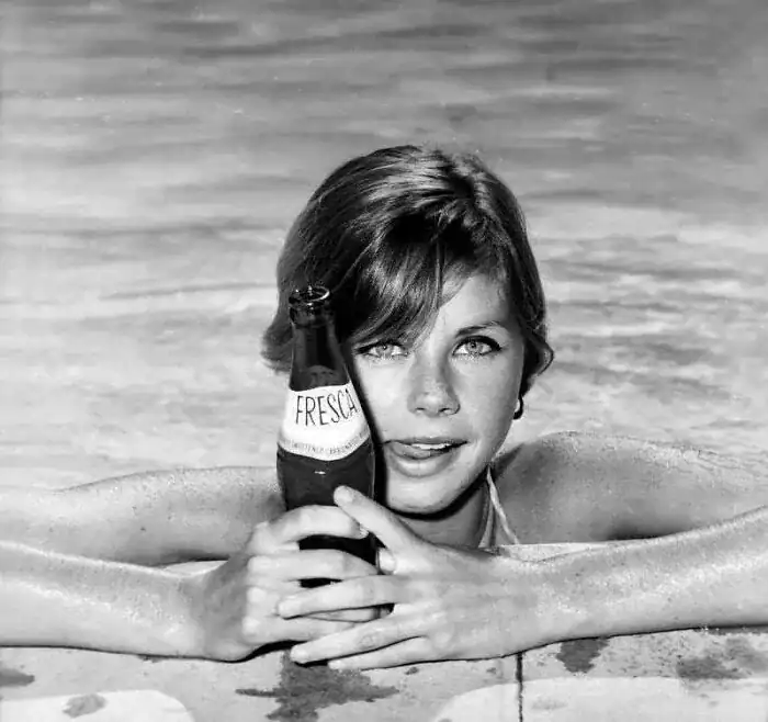 A black and white vintage Fresca soda advertisement featuring a woman holding a glass bottle while in a pool.