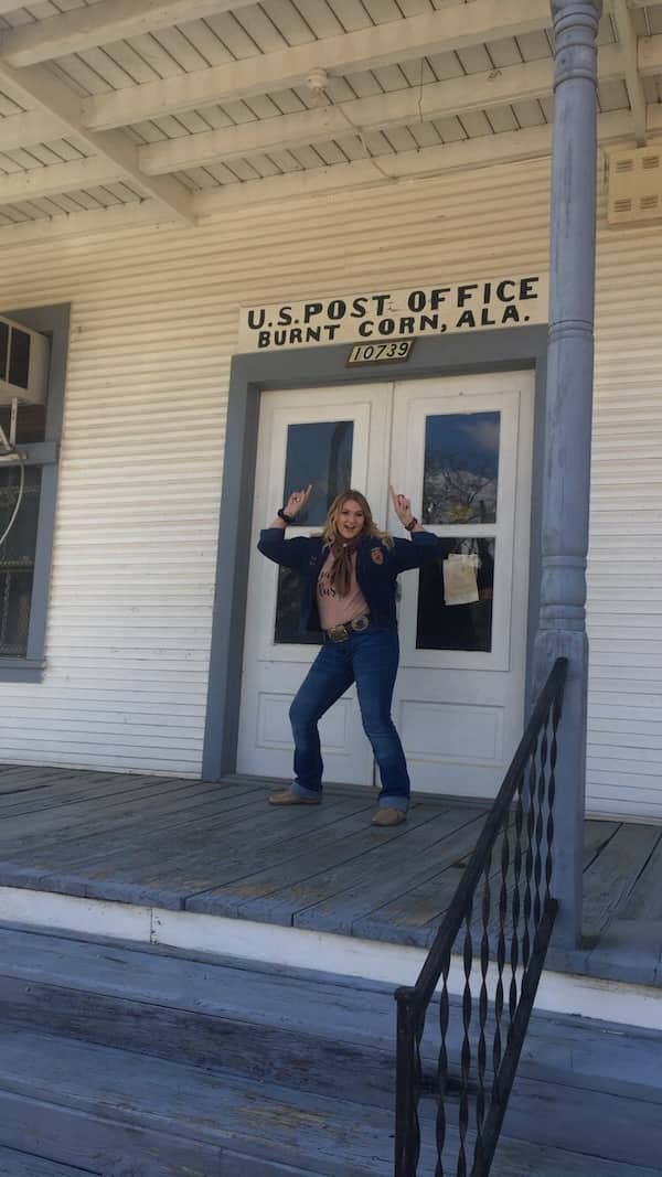 Woman posing in front of the Burnt Corn Alabama United States Post Office wooden building.