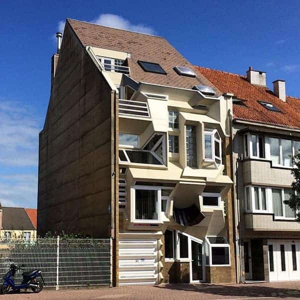 A chaotic Belgian apartment building with windows and balconies protruding at multiple jarring, irregular angles.