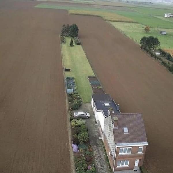 Aerial view of a thin Belgian house situated on a narrow strip of land amidst fields.