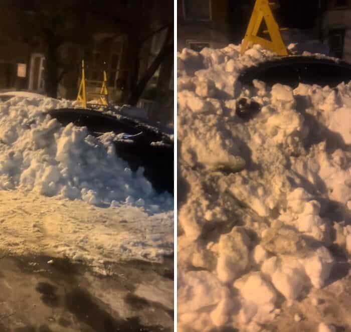 Dark car entombed in a wall of snow with a yellow ladder placed on top.
