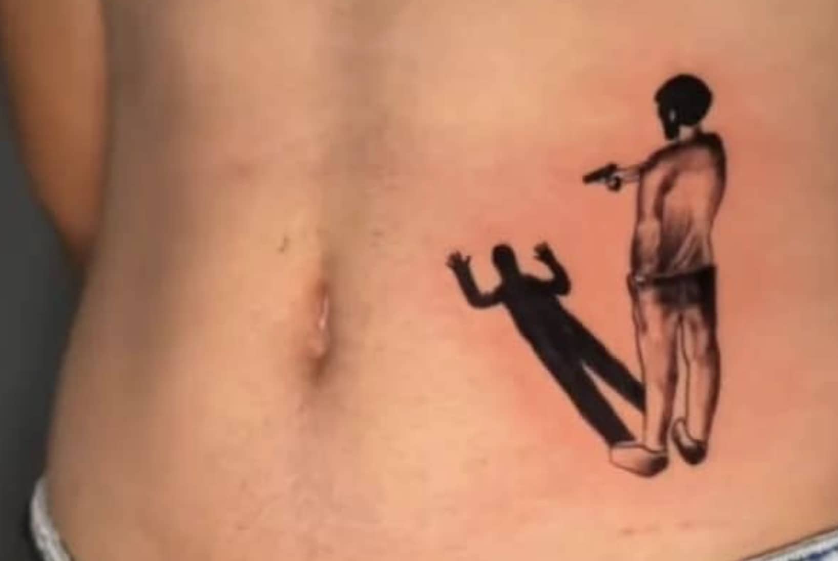 Humorous tattoo on a person's torso showing a man holding a gun toward his own shadow.
