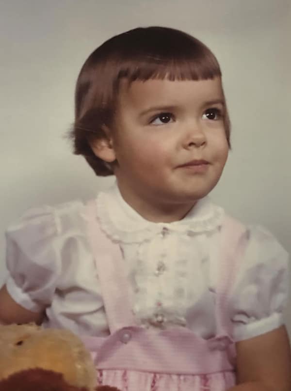 A toddler girl wearing an extreme version of the 80s haircut bowl cut. The hair is sleek and short, with "micro-bangs" cut high on the forehead and the rest of the hair falling in a sharp, blunt line around the ears.