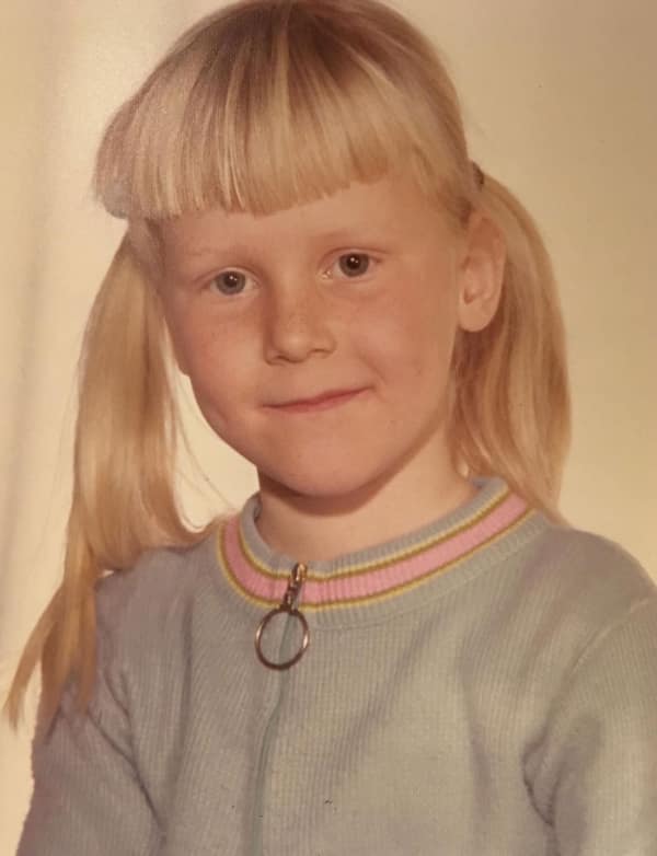 vintage school portrait of a young girl with a classic 80s haircut featuring high-sitting blonde pigtails and a thick, blunt-cut fringe that covers her entire forehead