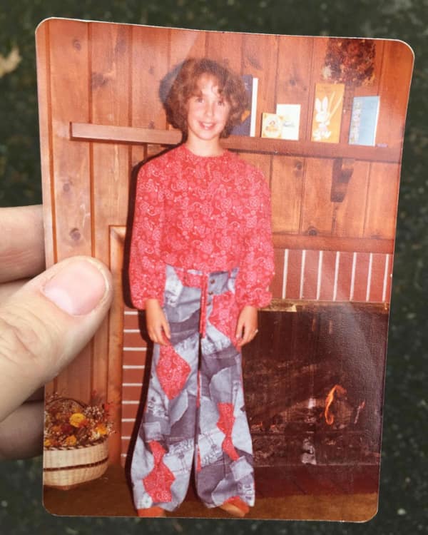 casual indoor photo of a young girl with a short, curly 80s haircut. The natural-looking perm or curl style is short and layered, reaching just to her chin, standing in front of a wood-paneled wall.