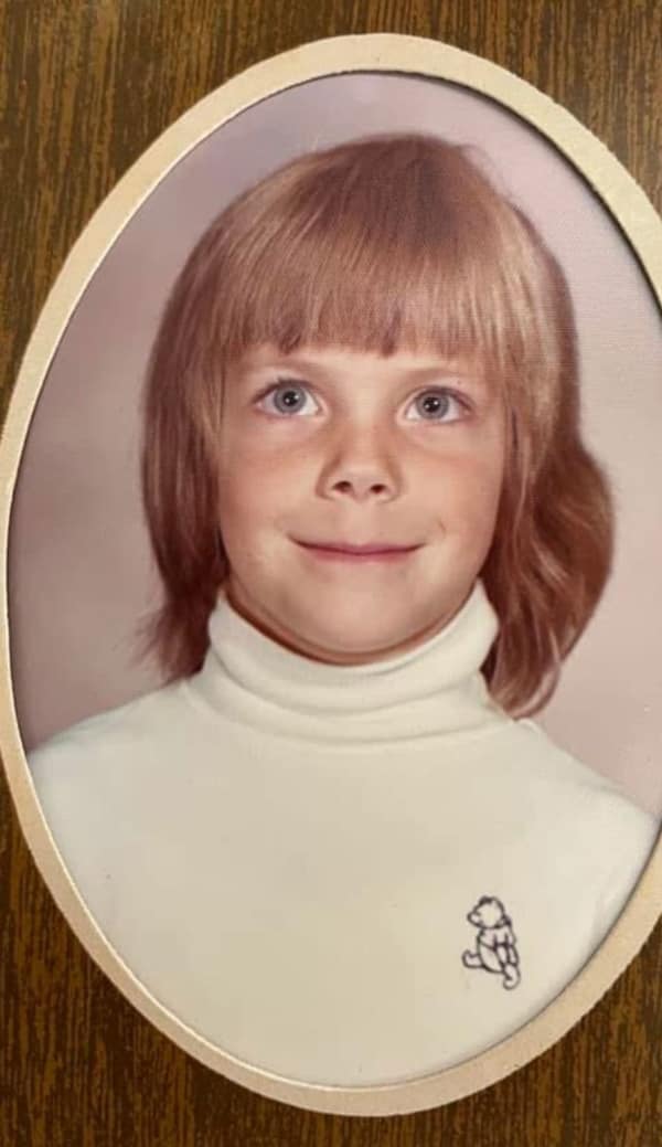 oval-framed school photo of a young girl with a layered blonde 80s haircut. The "shag" style includes thin, feathered bangs and soft layers that flip outward, a more subdued version of the decade’s high-volume trends.