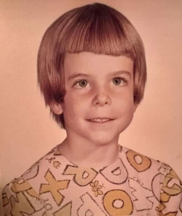quintessential 1980s school portrait of a young boy featuring a precision bowl cut. The hair is cut in a perfectly straight line around the head, creating a mushroom-like silhouette that was a staple of the era.