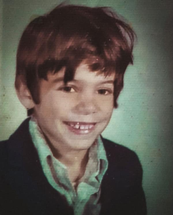 A school photo of a boy with a messy, feathered 80s haircut. The look features a voluminous, wind-swept top and sides, typical of the relaxed, shaggy styles popular for young men in the mid-80s.
