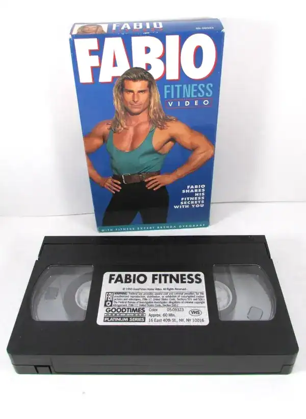peak fitness find in 90s pictures showcasing a pristine VHS copy of Fabio Fitness, featuring the iconic romance novel cover model posing confidently in a teal tank top and black leggings on the cardboard sleeve.