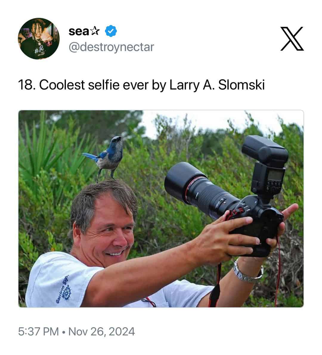 Titled "Coolest selfie ever" by Larry A. Slomski, this image shows a smiling photographer holding his professional camera with a flash while a vibrant blue bird perches calmly on the center of his head.