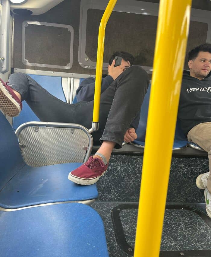 A textbook display of "main character syndrome" shows a passenger occupying three bus seats with their legs sprawled out while staring at their phone, a classic move for annoying people on public transit.