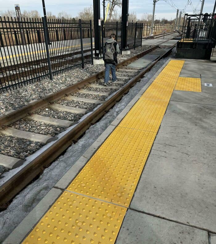 Safety protocols are completely ignored as a person walks directly down the center of the train tracks next to a platform, capturing the dangerous side of annoying people on public transit.