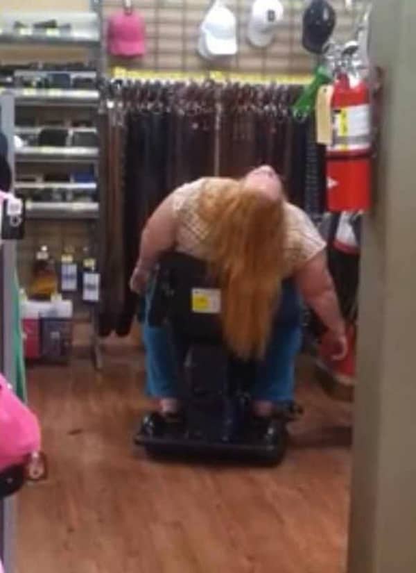 Woman with long hair slumped backward in a motorized shopping cart in the middle of a store aisle.