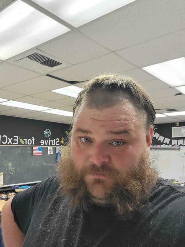 unfortunate bad haircut featuring a man in a classroom with a thick, bushy beard, but the top of his head is mostly shaved except for a sparse, thin fringe combed forward over his bald scalp.