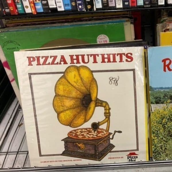 One of the best thrift store finds for music lovers: a "Pizza Hut Hits" vinyl record featuring a bizarre illustration of an old-fashioned gramophone with a pepperoni pizza serving as the record.
