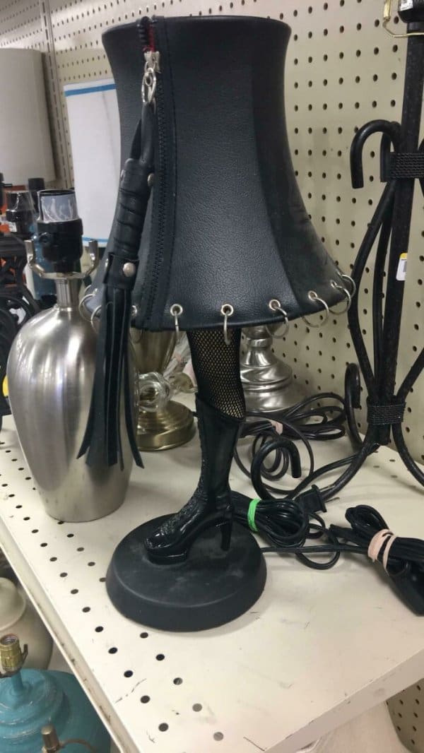The ultimate "Leg Lamp" parody found at a thrift shop: a black leather lampshade adorned with silver O-rings and a leather tassel, standing on a single mannequin leg wearing a fishnet stocking and a high-heeled lace-up boot.