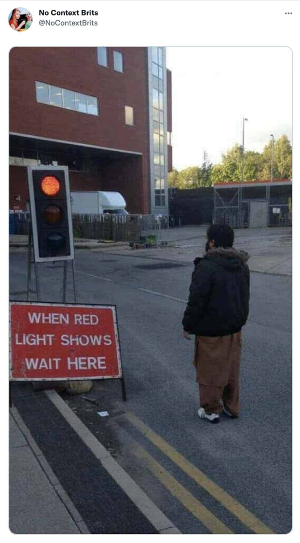 Obedient British man standing alone waiting at red pedestrian light in empty car park