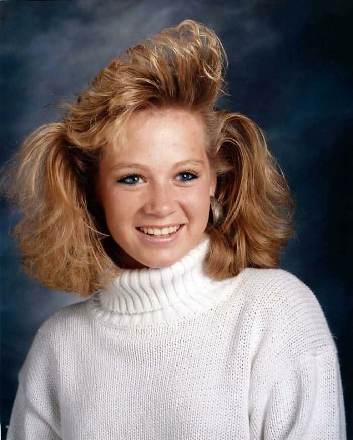 Young woman with blonde hair featuring a tall, vertical side-swept wave and voluminous curls.