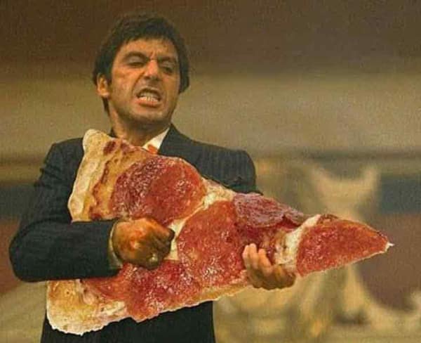 Al Pacino as Tony Montana in Scarface aggressively holding a massive giant slice of pepperoni pizza instead of a machine gun. A cinematic masterpiece food meme.