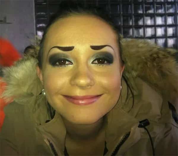 Smiling woman with thick dark eyebrows shaped like dramatic soaring bird wings over eyeshadow.