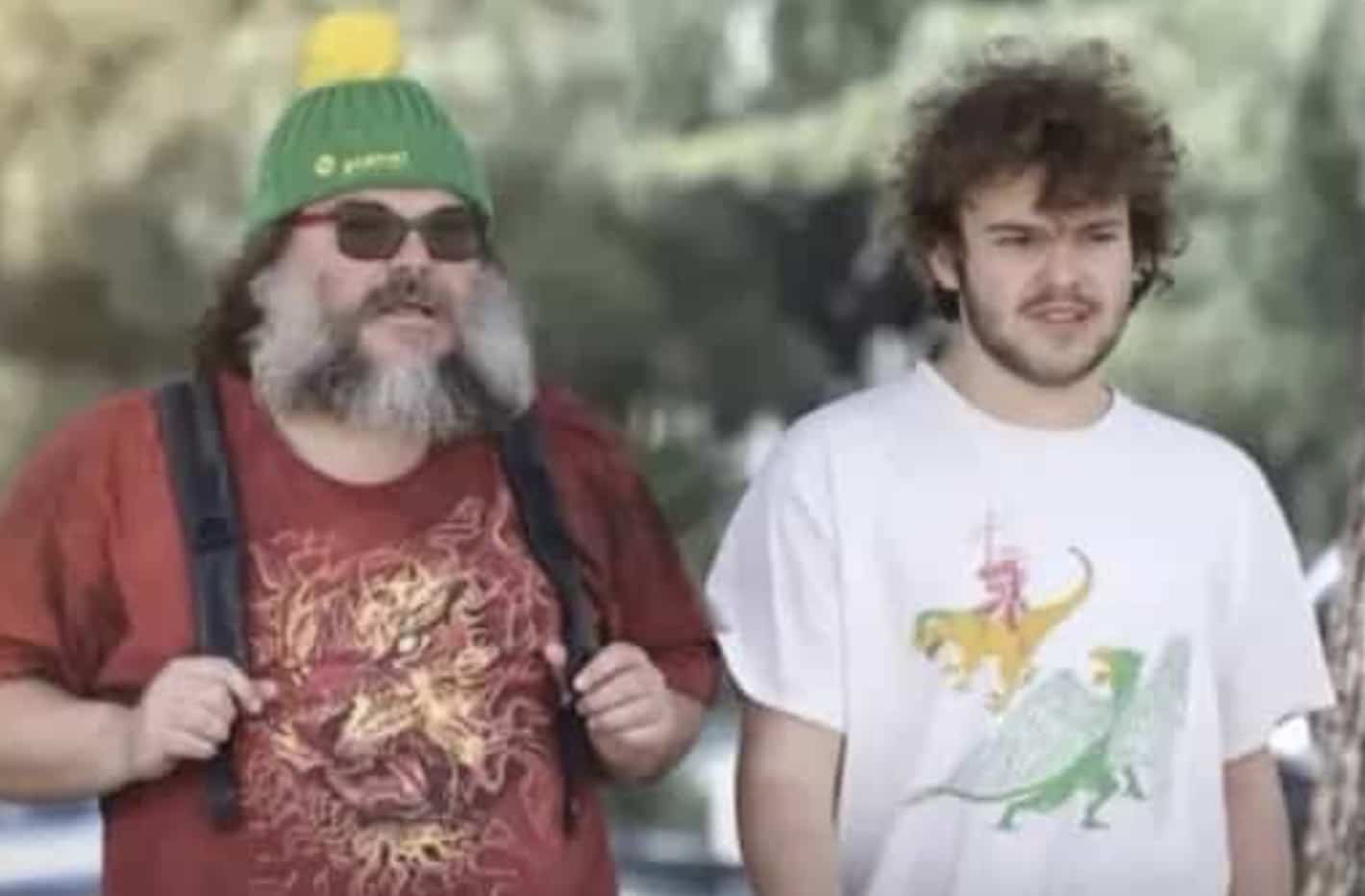 Actor Jack Black and his son walking together outdoors wearing casual graphic t-shirts and hats.