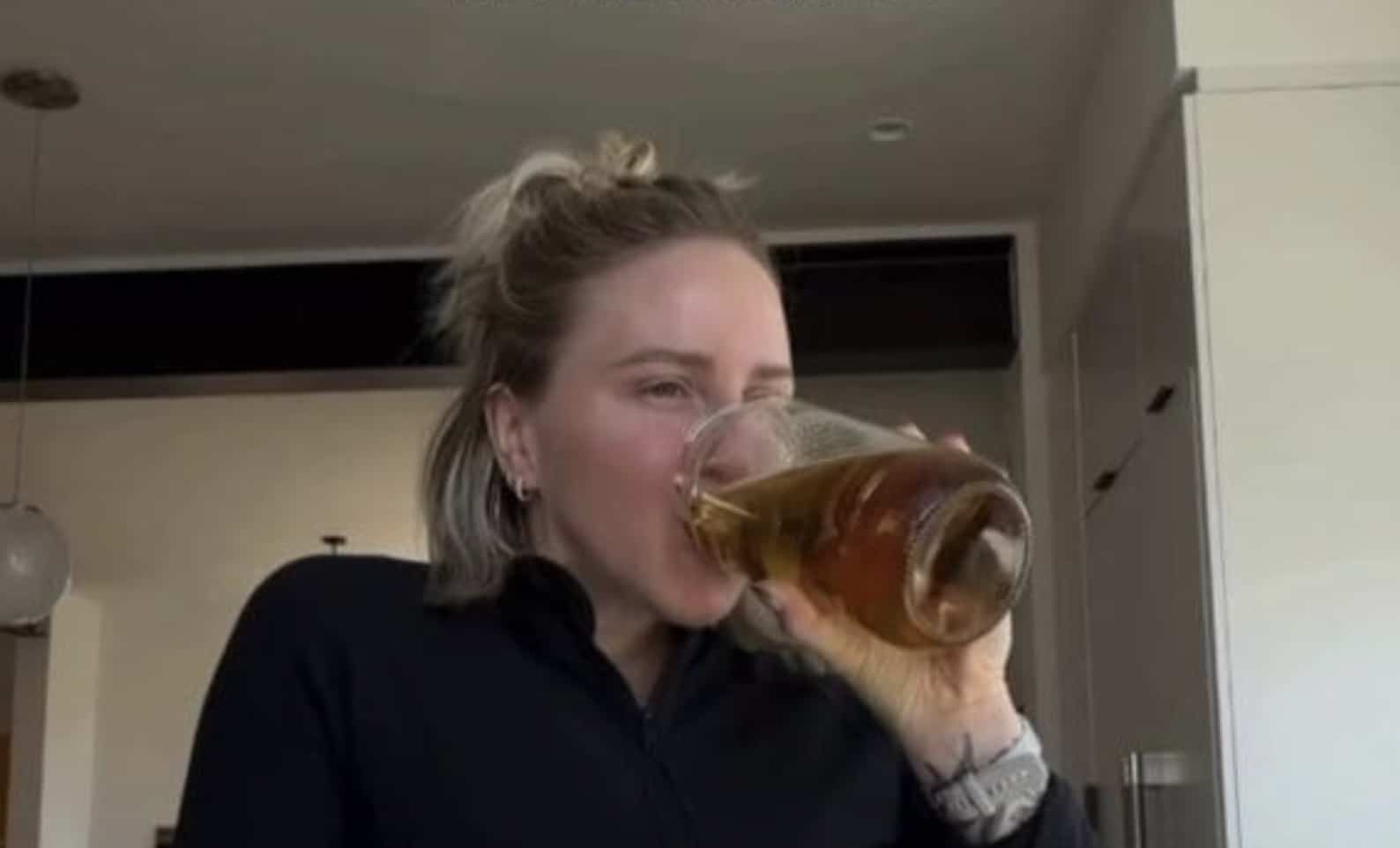 Woman drinking a large glass of iced tea in a kitchen, captured in a candid moment.