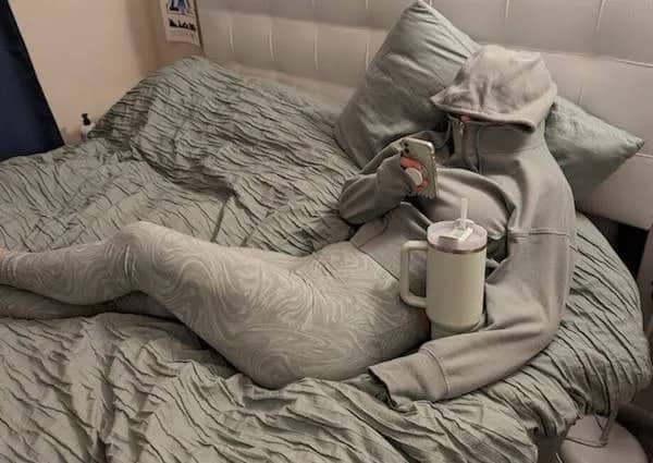Person wearing matching grey loungewear and a hoodie completely blended into grey bed sheets.