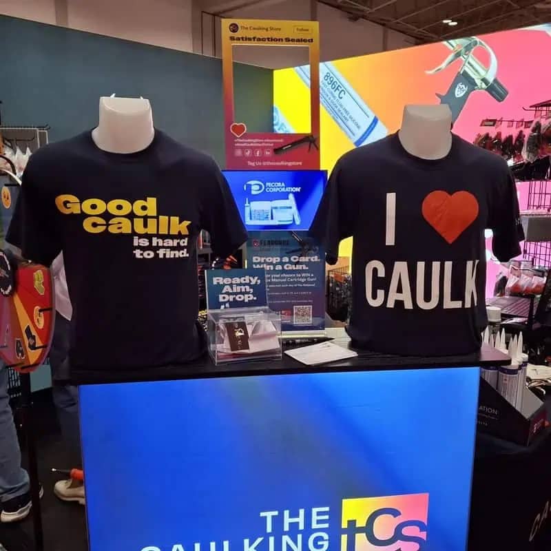 Trade show booth display with black t-shirts featuring puns about loving "caulk" for home improvement.