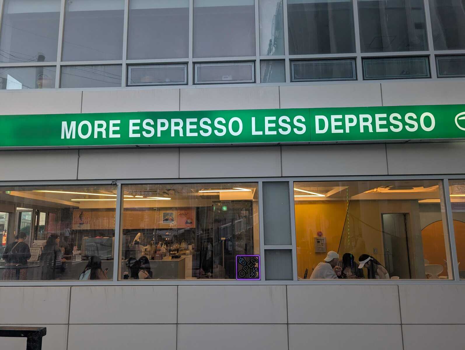 A modern cafe storefront sports a vibrant green banner with the rhyming, relatable slogan "MORE ESPRESSO LESS DEPRESSO" displayed above its windows.