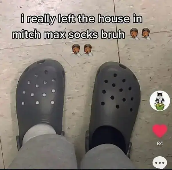 first-person view of a person wearing grey Crocs with one white and one black sock, accompanied by a caption with a funny spelling mistake calling them "mitch max socks" instead of "mismatched."