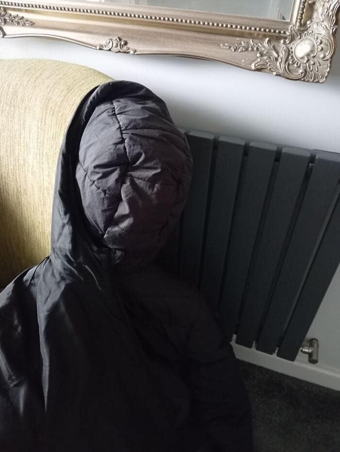 creepy optical illusion in this collection of inanimate objects with faces, showing a black puffer jacket draped over a chair that creates an eerie, textured face looking directly at the camera.